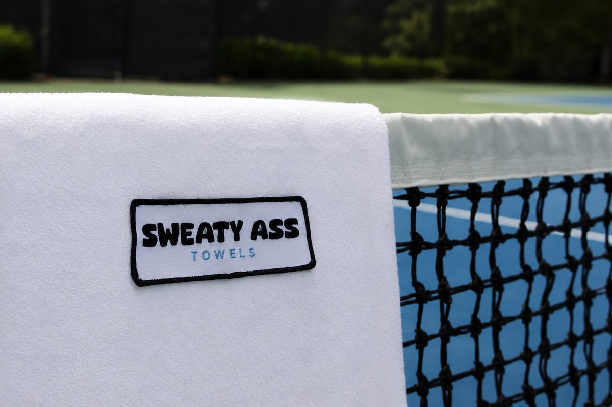 Sweaty Ass Towel in white draped over a tennis net